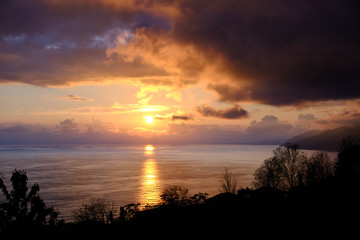 Sunset over the sea. Big orange clouds over mountains and water. Coastline. Storm off shore. Evening light.