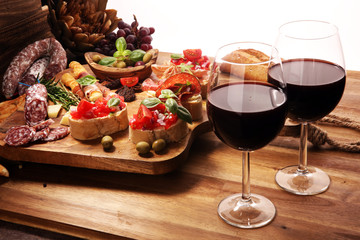 Traditional italian antipasto bruschetta appetizer with cherry tomatoes, cream cheese, basil leaves and balsamic vinegar on cutting board with prosciutto, salami, cheese