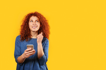 Thoughtful redhead woman with mobile phone on color background