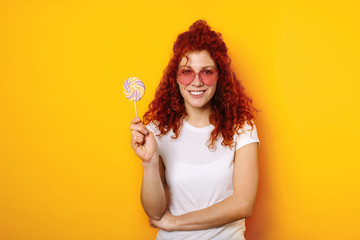 Beautiful redhead woman with lollipop on color background