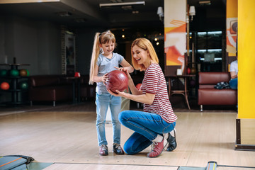 Woman and her little daughter playing bowling in club
