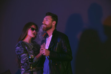 Young couple smoking hookah on dark background