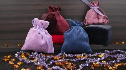 Multicolored velvet bags for jewelry and velvet box placed on a wooden shelf against the background of amber beads and amethyst beads - Powered by Adobe