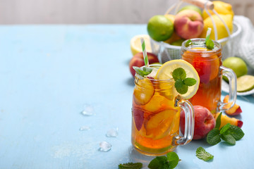 Iced tea with peaches, lemons, limes and mint with ice cubes, summer refreshment drink, copy space background
