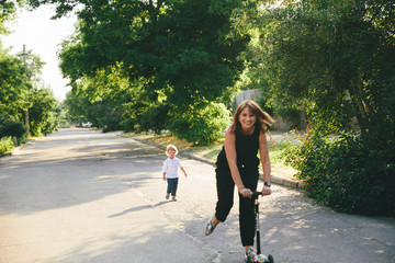 young mother is riding a scooter and a little son behind her.