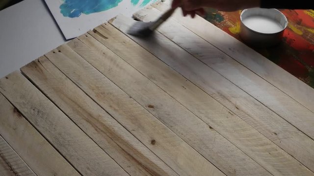 Decorator covers by paintbrush wooden planks surface with water-based undercoat, used on wood