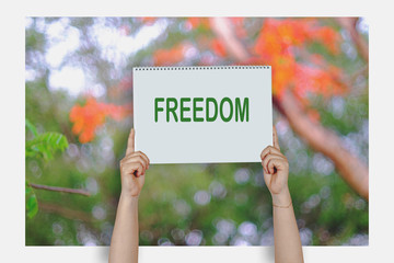 Woman hands holding high a post card that says FREEDOM against a blur nature.