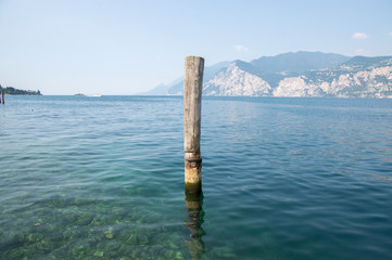 Wooden bricole for boats in the water, lake Lago Di Garda, morning light, mountains on the background