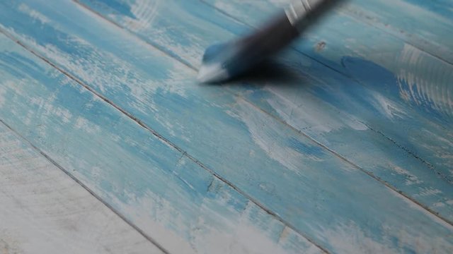 Decorator covers by paintbrush wooden planks surface with white and turquoise paint 