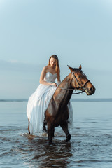 Obraz premium Beautiful girl in a white long dress riding a horse. Bride in the lake on horseback.