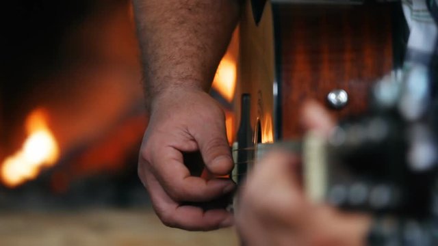 Closeup of hands playing guitar in front of a fireplace, side view