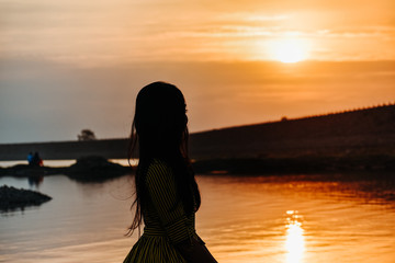 Fototapeta premium a beautiful girl standing in front of calm water and beautiful sunset sky at nyari dam, rajkot, India. 