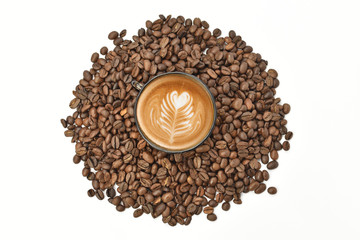 A cup of cappuccino on a white table, roasted coffee grains are scattered around a cup