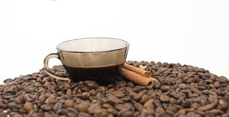 A cup of coffee on a white table, around a cup scattered grains of roasted coffee and fresh cinnamon