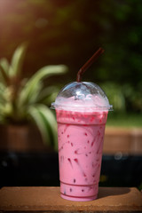 Iced pink fresh milk in plastic cup on garden background.