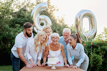 Family celebrating a  60th birthday, with balloons and cake, happy, cheering  - Powered by Adobe