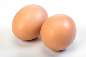 Two chicken brown eggs are close on a white background.