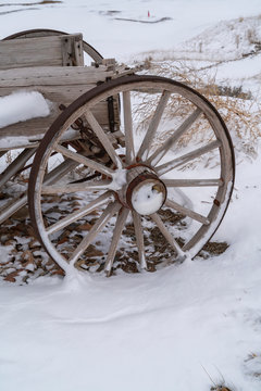 Wheel of an old wooden cart against a rocky snow covered terrain in winter