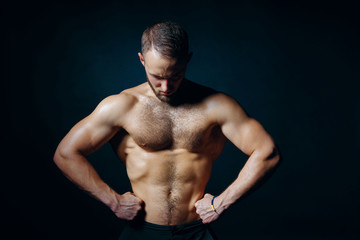 Fototapeta premium Low key portrait of muscular shirtless man at dark background