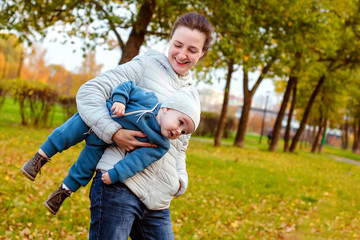 Naklejka na ściany i meble Happy loving family in the park. Mother in white and baby boy in blue having fun, playing and laughing in nature.