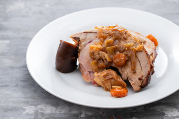 baked turkey leg with vegetables, smoked sausage and herbs on white dish