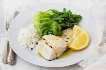 boiled cod fish with rice and vegetables on white plate