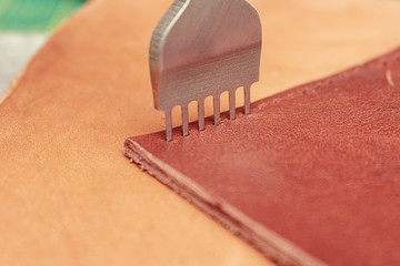 Punching holes in a leather wallet with line piercer diamond shape puncher tool before stitching handmade leathercraft