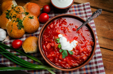 Ukrainian national cuisine - red borsch with donuts in a clay bowl on a wooden table.