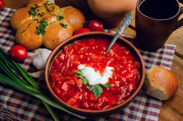 Ukrainian national cuisine - red borsch with donuts in a clay bowl on a wooden table.
