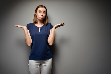 Don't know! Confused young woman against grey wall.
