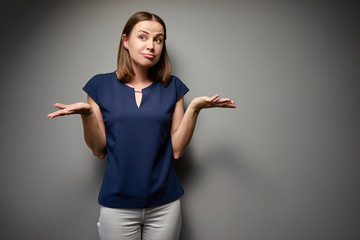 Don't know! Confused young woman against grey wall.