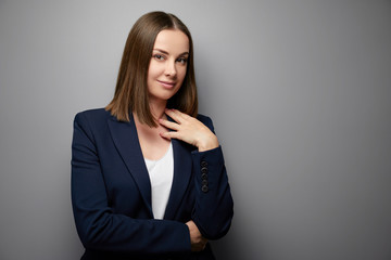 Confident young business woman in suit looking at camera. Grey background with copy space.