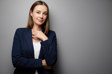 Confident young business woman in suit looking at camera. Grey background with copy space.