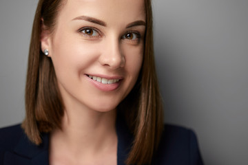 Close up studio portrait of oung businesswoman in suit looking at camera. Grey background.