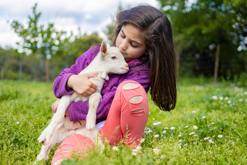 Little girl hugging a goat  on a field