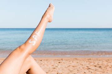 Raised up female leg with spf word made of sun cream at the beach. Sun protection factor concept