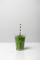 tasty, green and organic smoothie in glass with straw on grey
