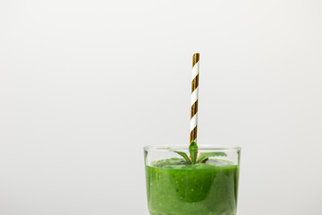 tasty, green and organic smoothie in glass with straw on white