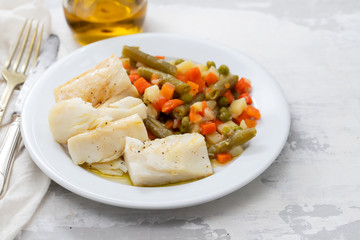 boiled cod fish with boiled vegetables on white plate on ceramic background