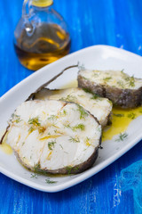 boiled fish with olive oil in white dish on blue wooden background