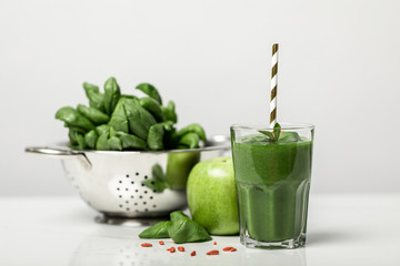 selective focus of green smoothie in glass with straw near spinach leaves and apple on white