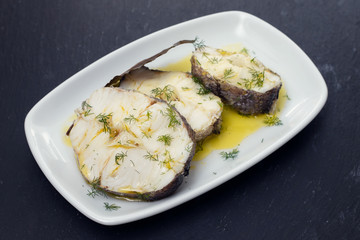 boiled fish with olive oil in white dish on ceramic background