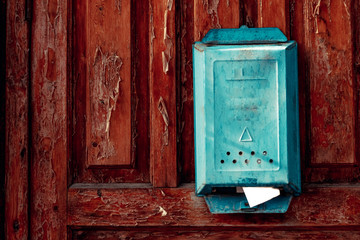 a turquoise vintage mailbox hangs on the weather-shattered door with shabby red paint