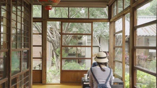 beautiful japanese style wooden house with green spring teien garden. back view two asian woman friends sitting in corner doing chado ceremony chatting sitting on floor. girls talking relaxing enjoy