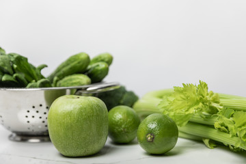 selective focus of sweet apple near green limes and cucumbers on white