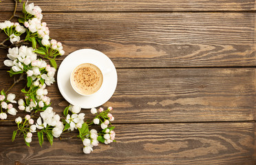 Fototapeta na wymiar A cup of hot aromatic coffee and a blossoming branch of an apple tree on a wooden background. Flat layout. View from above. Copy space.