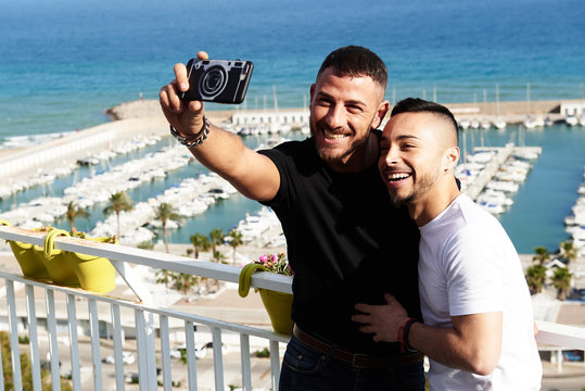 Una pareja gay se hace un selfie en el balc&oacute;n con el puerto detr&aacute;s de ellos en un d&iacute;a de verano
