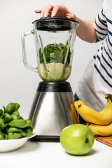 cropped view of woman using blender near organic fresh fruits on white