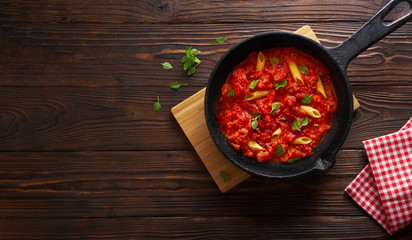 Pasta penne with tomato sauce and basil on iron cast pan. Wooden table, top view with copy space