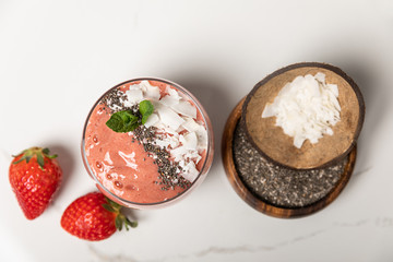 top view of tasty smoothie with coconut flakes in glass near tasty strawberries on white